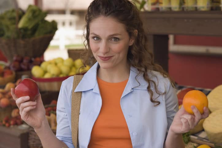 a young woman holding an apple and an orange