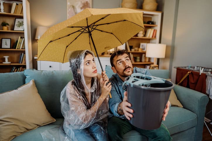 young couple catching water from ceiling leak